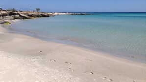 Une plage de sable fin bordée d’une eau turquoise et transparente, avec des affleurements rocheux.