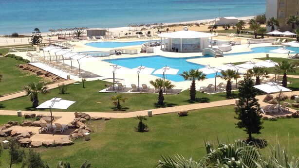 Un complexe hôtelier doté d’une grande piscine centrale, de plusieurs piscines plus petites et d’une zone de plage.