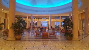 Un hall d’entrée spacieux avec un espace salon central, de grandes colonnes et des plantes en pot.