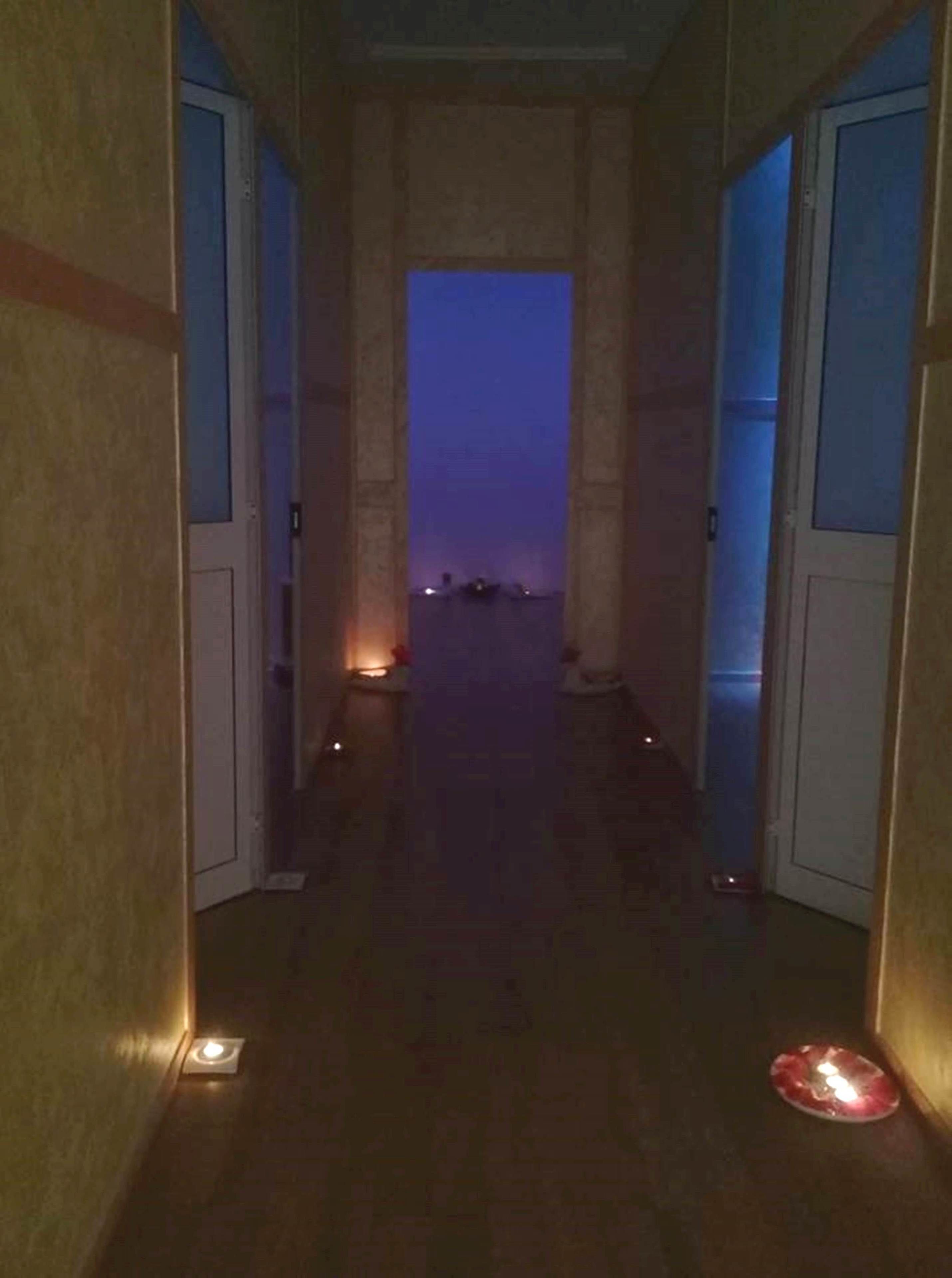 A hallway with doors leading to rooms, a dimly lit corridor, and a view of the sea at dusk.