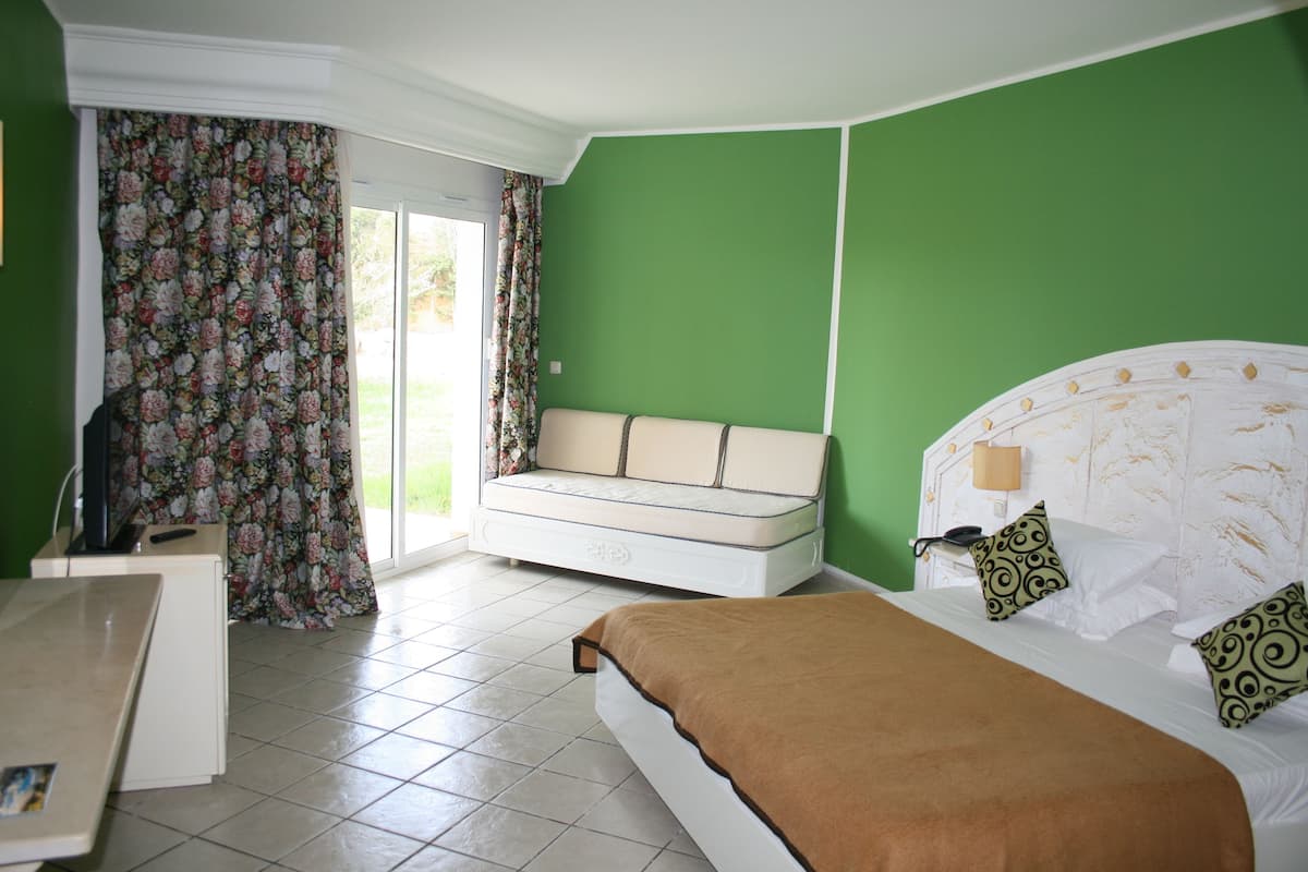 A bedroom with a bed, a sofa, a desk, and a window with curtains.