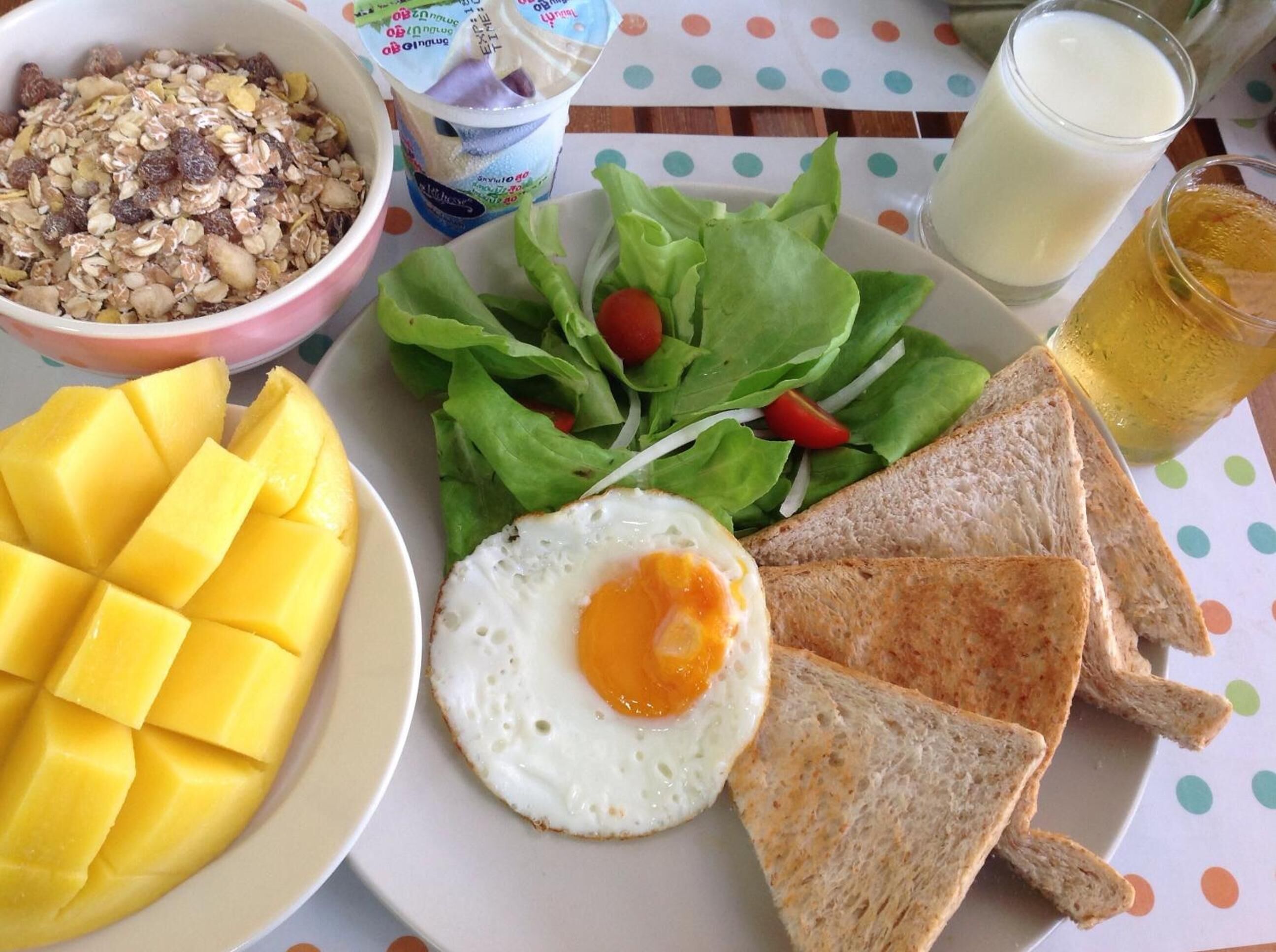 En morgenmadstallerken med ristet brød, spejlæg, mango, salat og yoghurt.