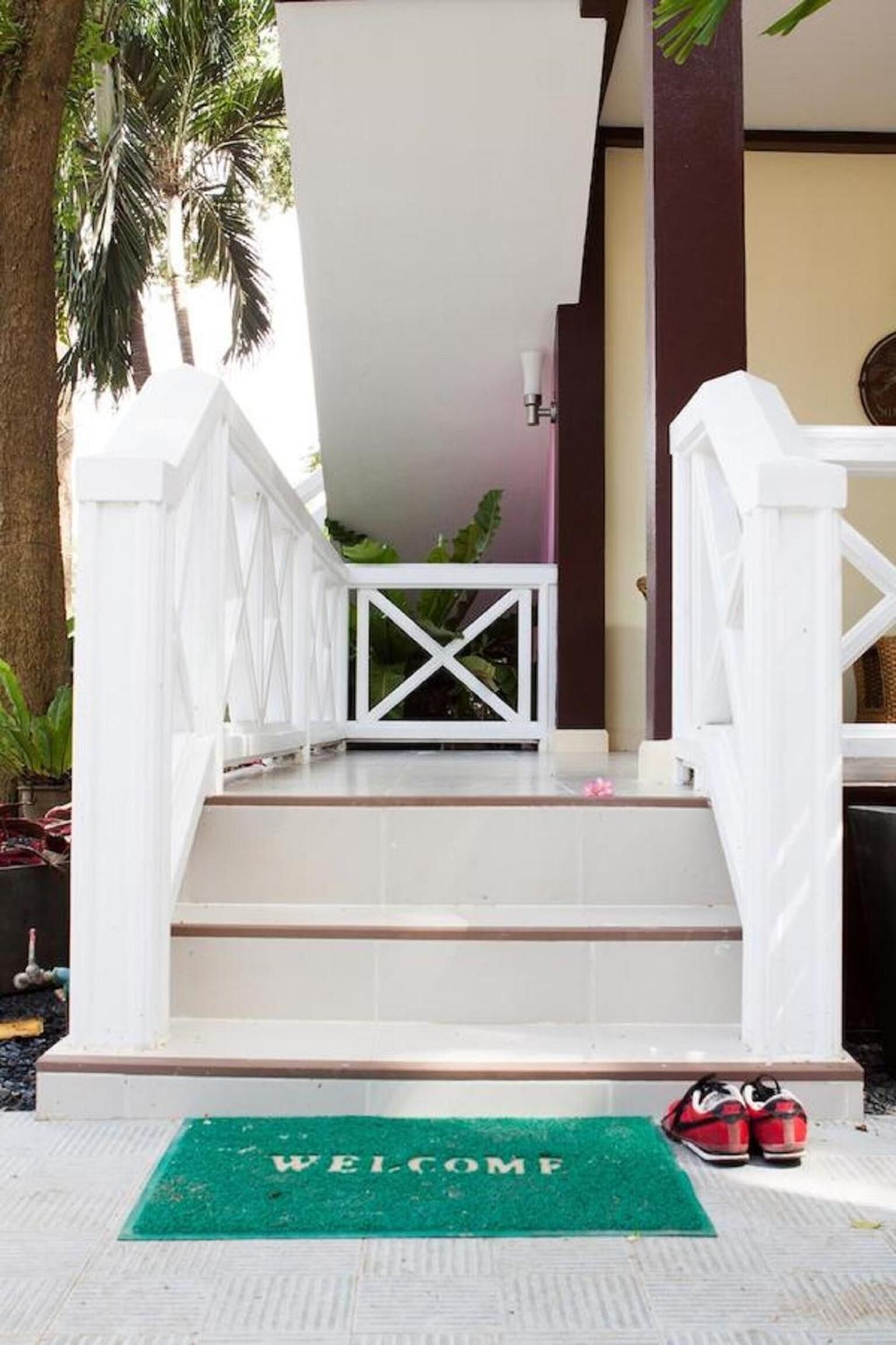 A staircase with a white railing, a green welcome mat, and a pair of red shoes on the steps.
