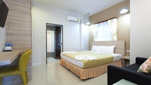 A hotel room with a bed, a desk, a chair, a TV, and an air conditioning unit. - Sandy House Rawai (Rawai)