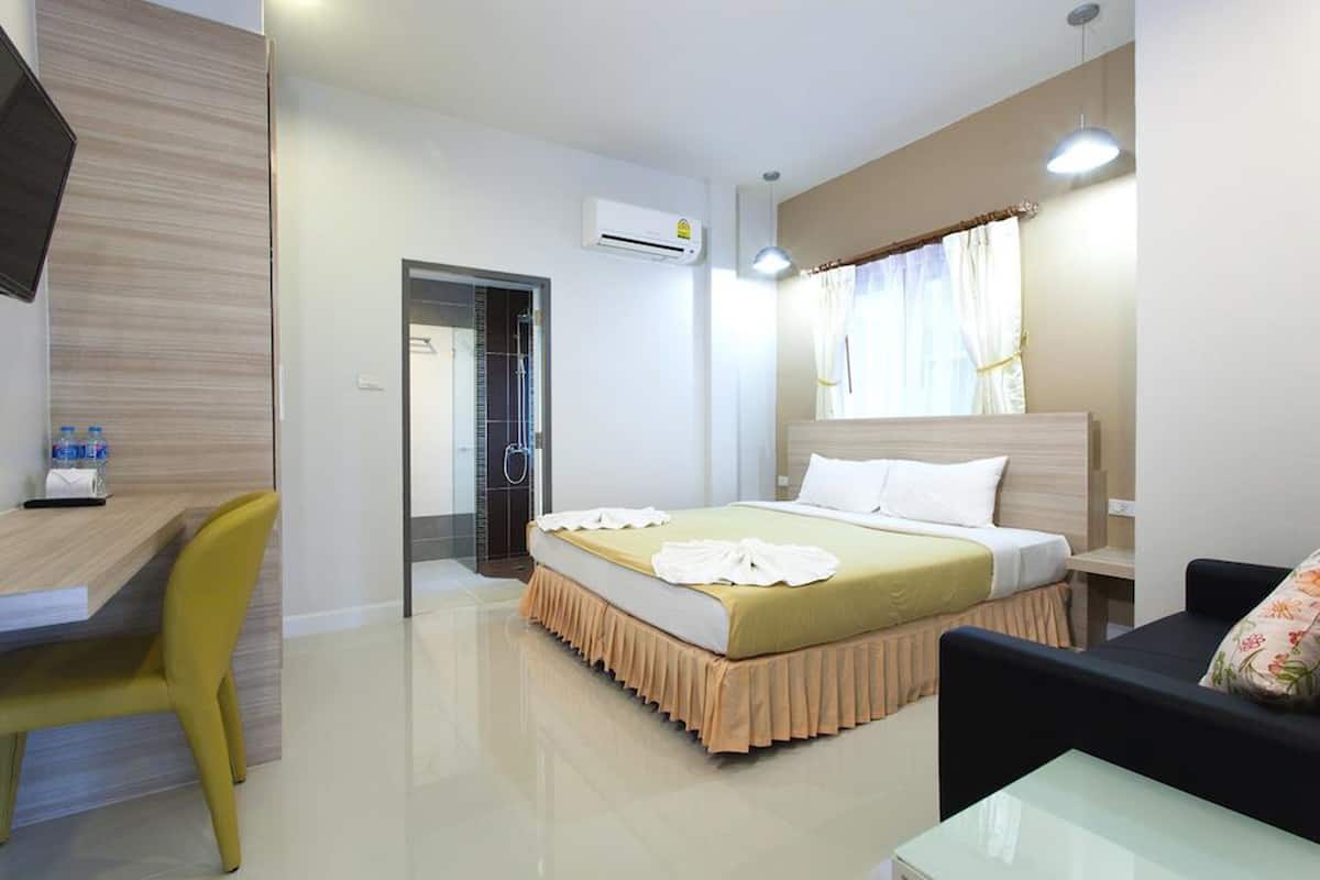 A hotel room with a bed, a desk, a chair, a TV, and an air conditioning unit.