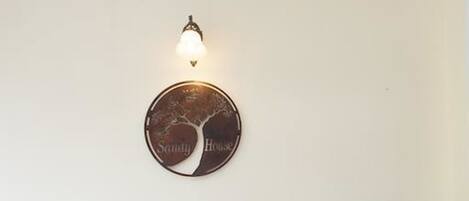 A black leather armchair with wooden legs and a tufted backrest, positioned in front of a wall-mounted round mirror with a tree design and the words "Sunny House" below it.