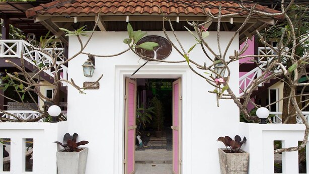 A white building with a tiled roof, a pink door, and potted plants. - Sandy House Rawai (Rawai)