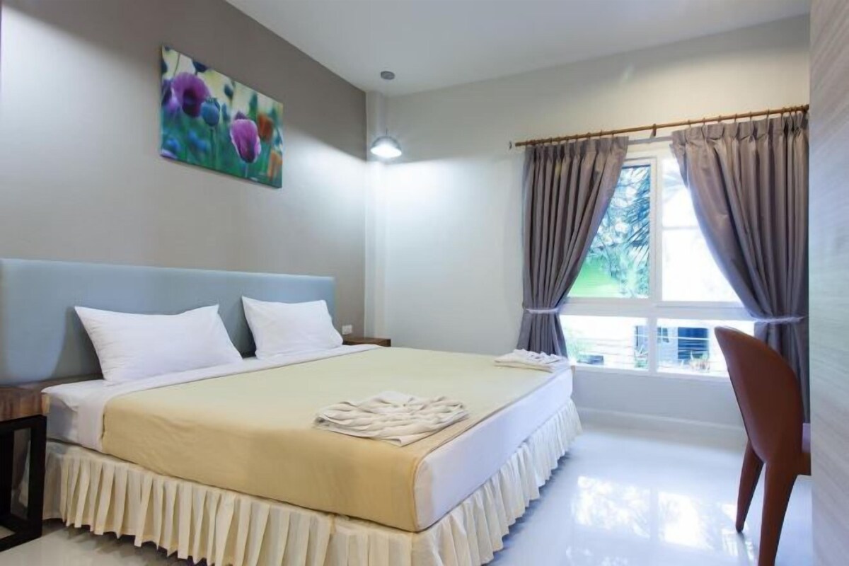 Un dormitorio con una cama, un cuadro, una ventana con cortinas y una silla.
