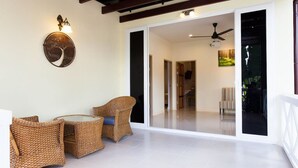 A spacious balcony with wicker furniture, a ceiling fan, and a sliding glass door leading to an interior space. - Sandy House Rawai (Rawai)