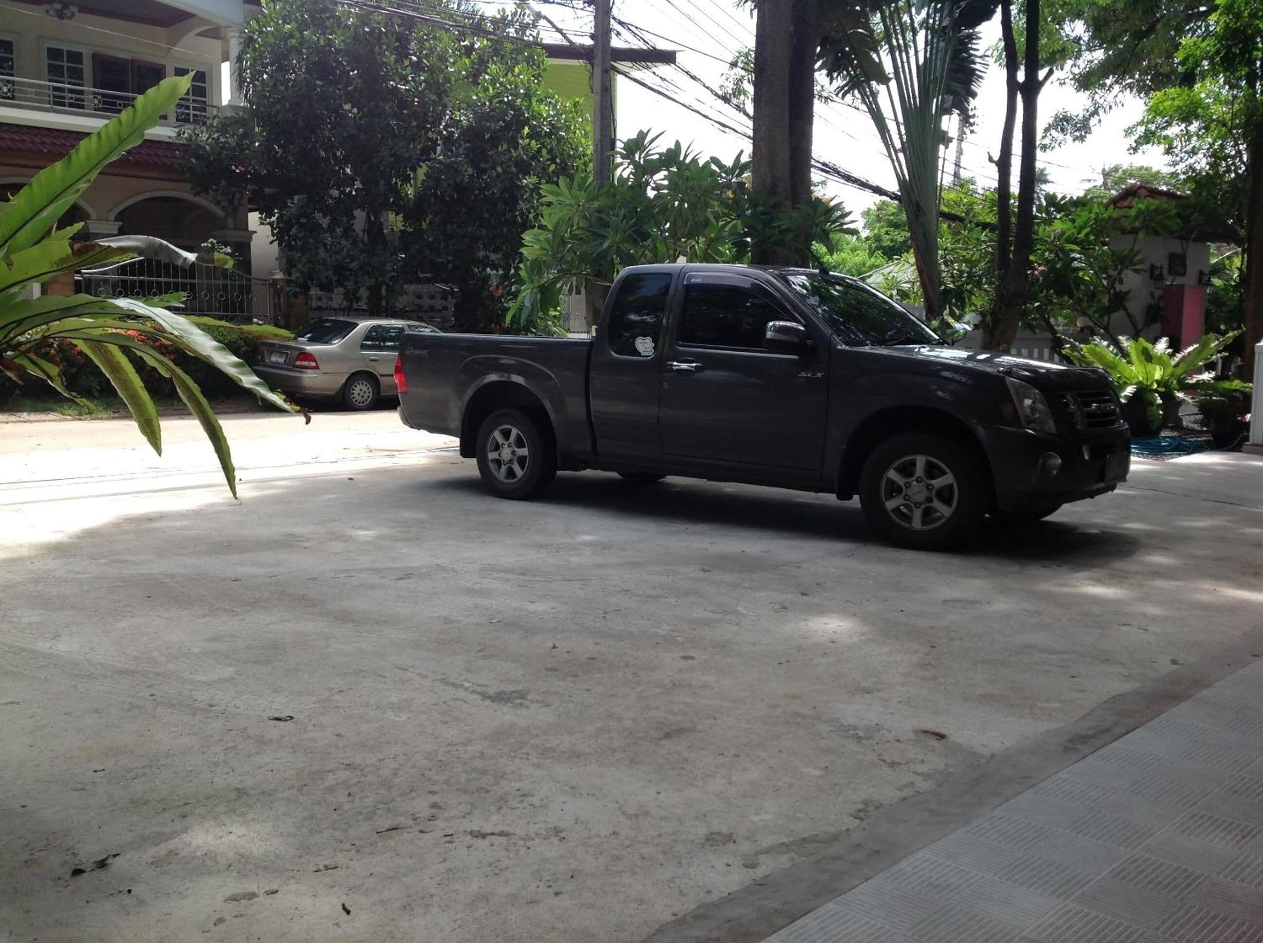 A dark-colored pickup truck parked on a concrete surface with a building and trees in the background.
