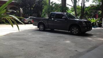 A dark-colored pickup truck parked on a concrete surface with a building and trees in the background.