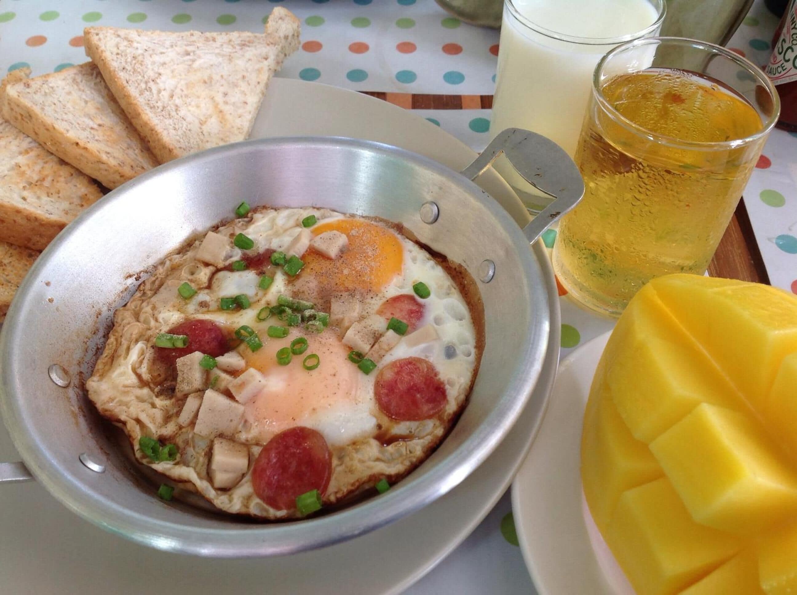 A breakfast plate with scrambled eggs, sausage, and green onions, accompanied by toast and a glass of juice.