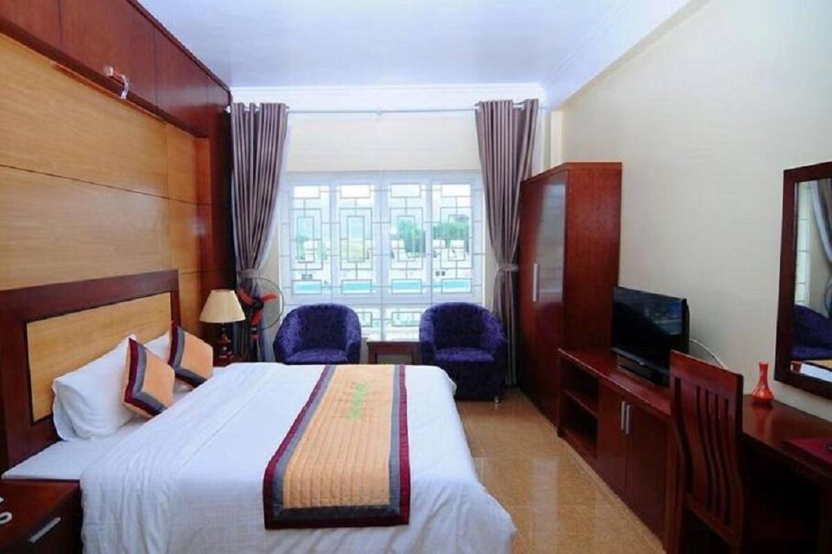 A hotel room with a bed, a desk, a chair, a TV, and a window with curtains.