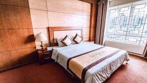 A hotel room with a large bed, a nightstand, a lamp, and a window with a geometric pattern. - Thao Nguyen Hotel (Thao Nguyen)