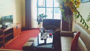 A living room with a TV, sofa, coffee table, and a large window with curtains. - Thao Nguyen Hotel (Thao Nguyen)