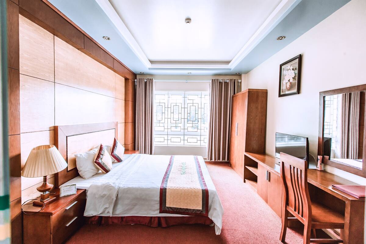 A hotel room with a large bed, a desk, a television, and a window with curtains.