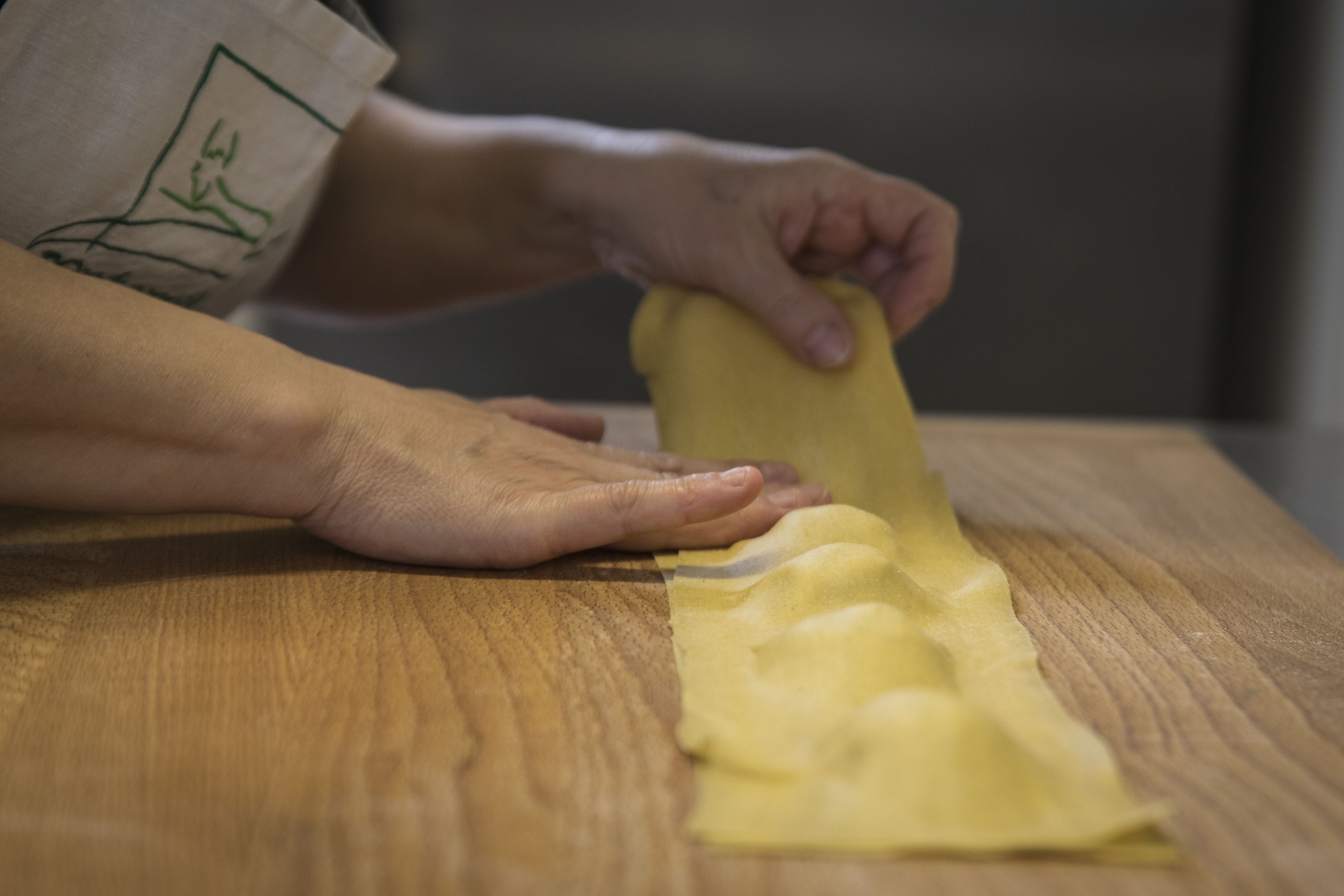 A person peeling a yellow potato on a wooden table.