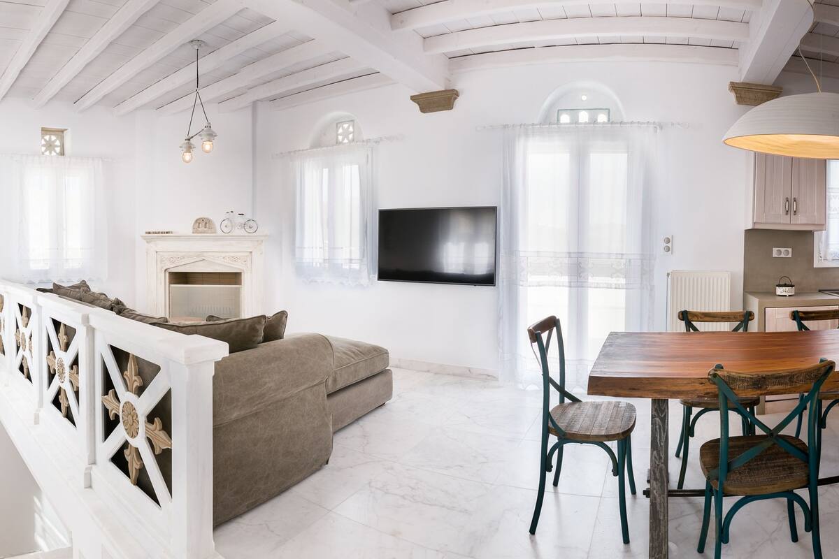 A spacious living room with a fireplace, a dining area with wooden chairs, and a kitchen with white cabinets and an orange refrigerator.