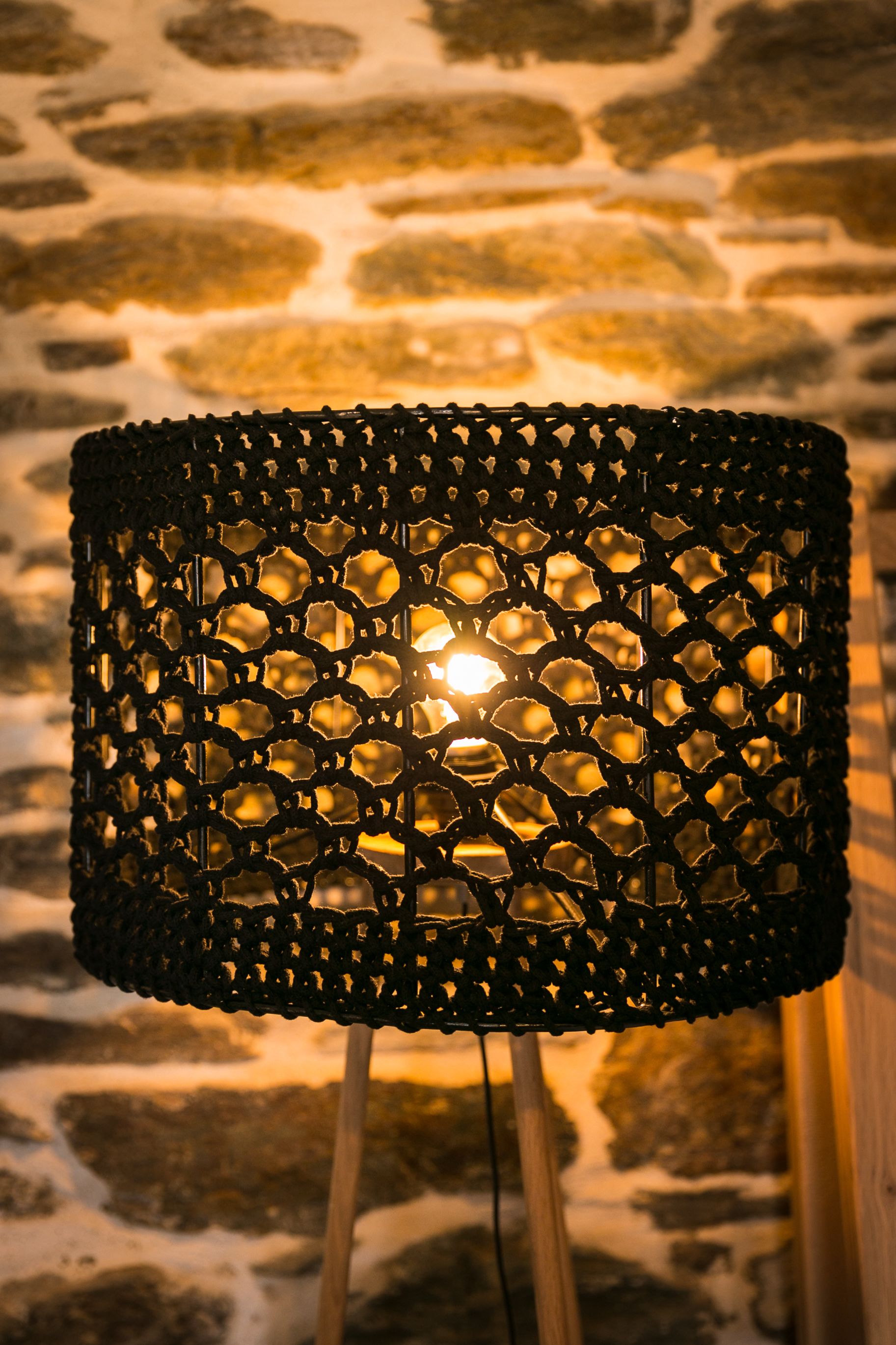 A decorative lamp with a geometric pattern, mounted on a stand against a stone wall.