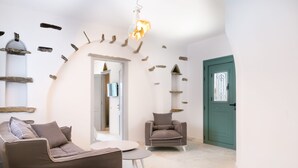 A modern living room with a sofa, armchair, and a small round table. There is a teal door and a white wall with decorative elements. - imarkellis boutique villas (Tinos)