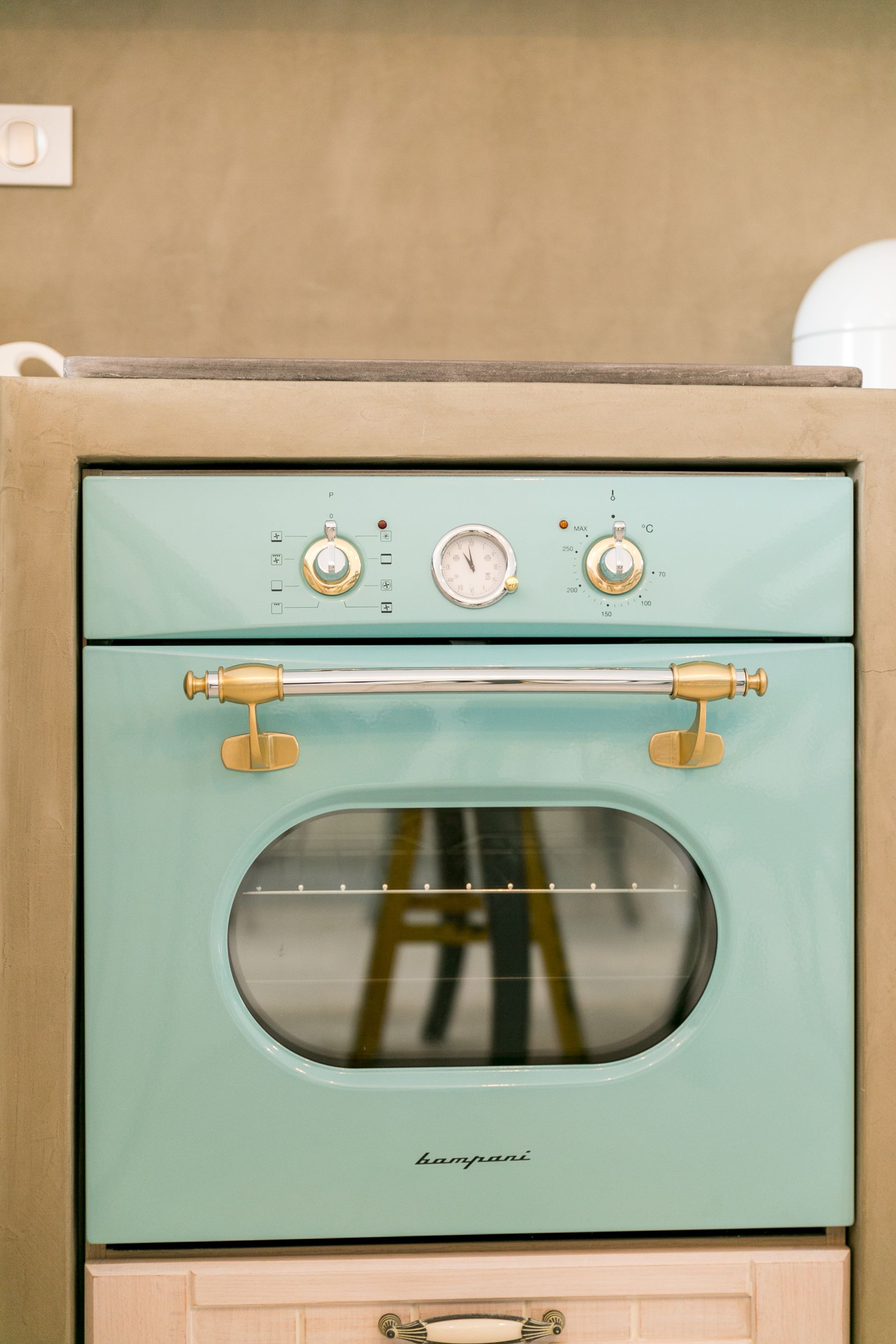 A vintage teal oven with brass fixtures and a control panel.
