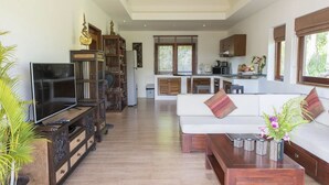 A spacious living area with a TV, bookshelves, a sofa, and a coffee table. - Tropical Season Villa Resort (Koh Samui)