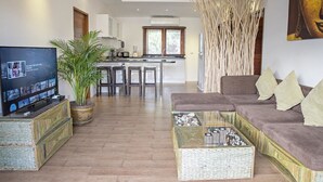 A modern living room with a sofa, a coffee table, a TV, and a kitchen in the background. - Tropical Season Villa Resort (Koh Samui)
