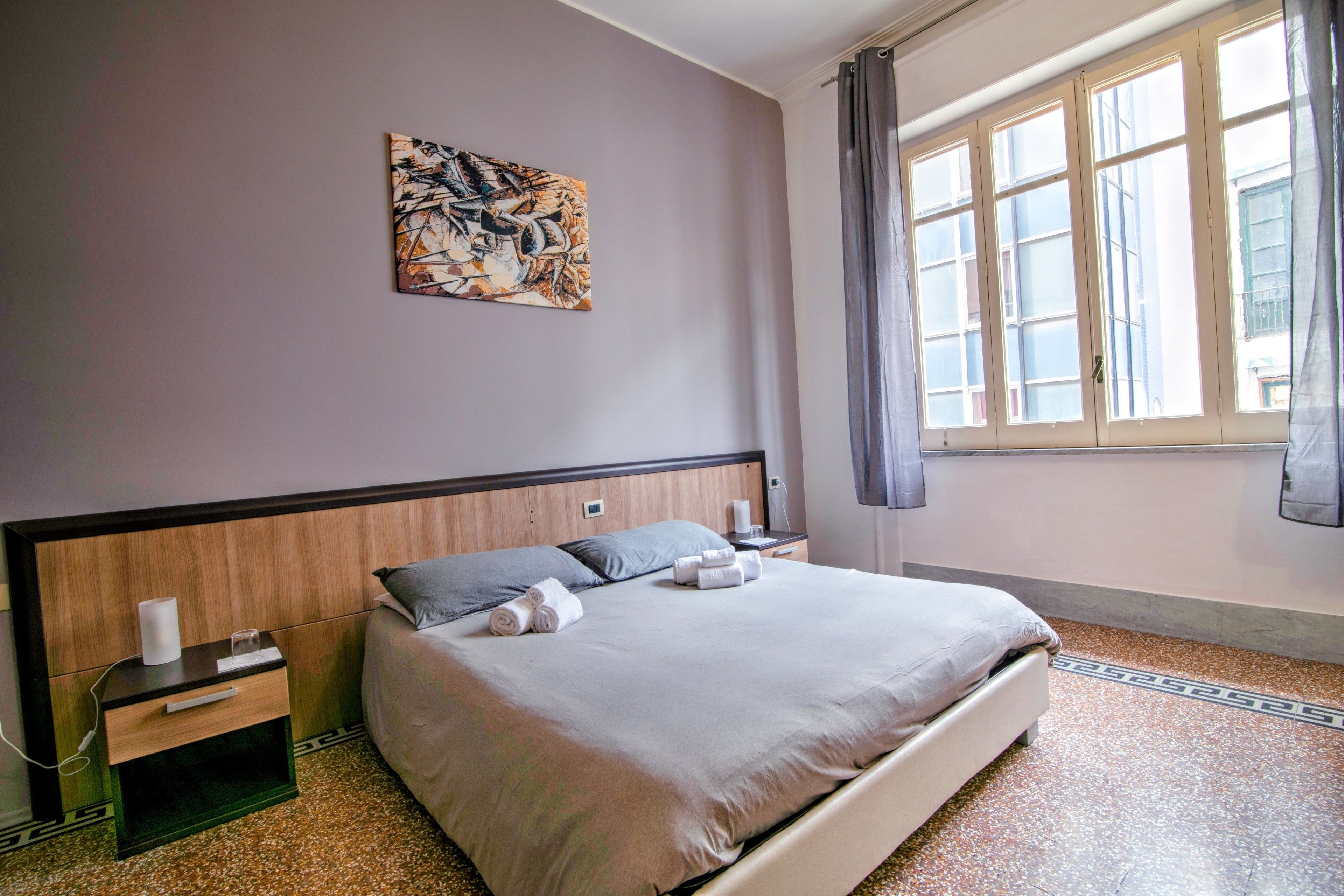 Un lit bien fait, avec des oreillers et des serviettes, une table de chevet avec une lampe, un tableau décoratif au mur et une fenêtre avec des rideaux.