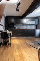 Una cocina moderna con armarios oscuros, piso de madera y una mesa de comedor de vidrio.