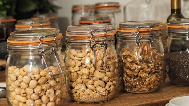 Un estante de madera con varios frascos de vidrio que contienen nueces y granos de diversos tipos.
