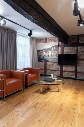 Un salon moderne avec un canapé en cuir, une table basse en verre et un mur en briques orné d’une fresque représentant un paysage urbain.