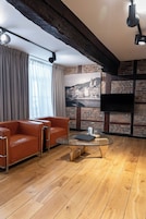 Una sala moderna con un sofá de cuero, una mesa de centro de vidrio y una pared de ladrillo con un mural de un paisaje urbano.