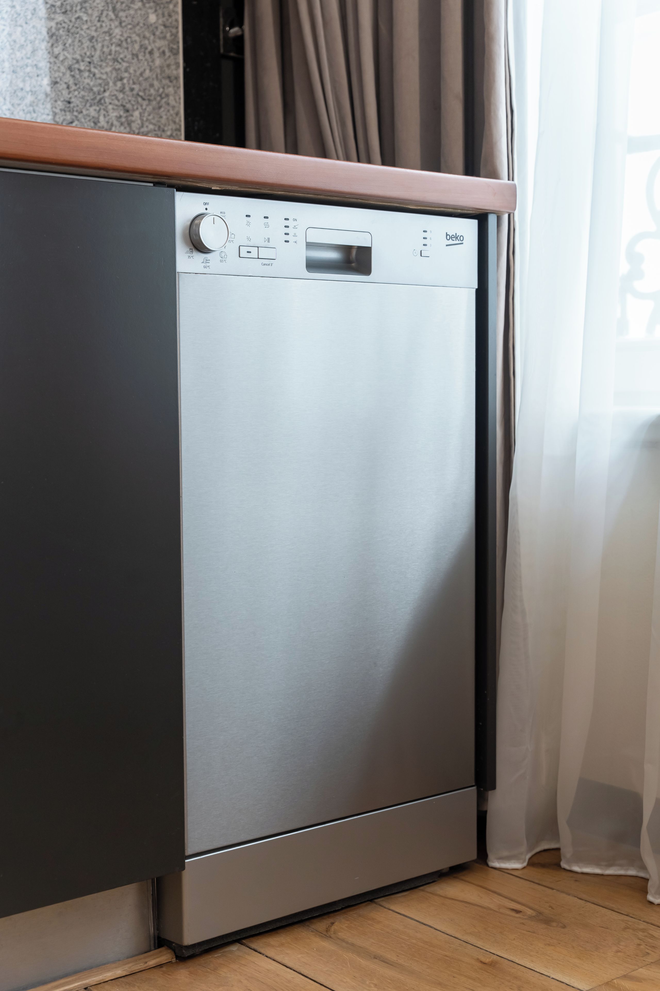Una cocina moderna con lavavajillas integrado, encimera de madera y una ventana con cortinas translúcidas.