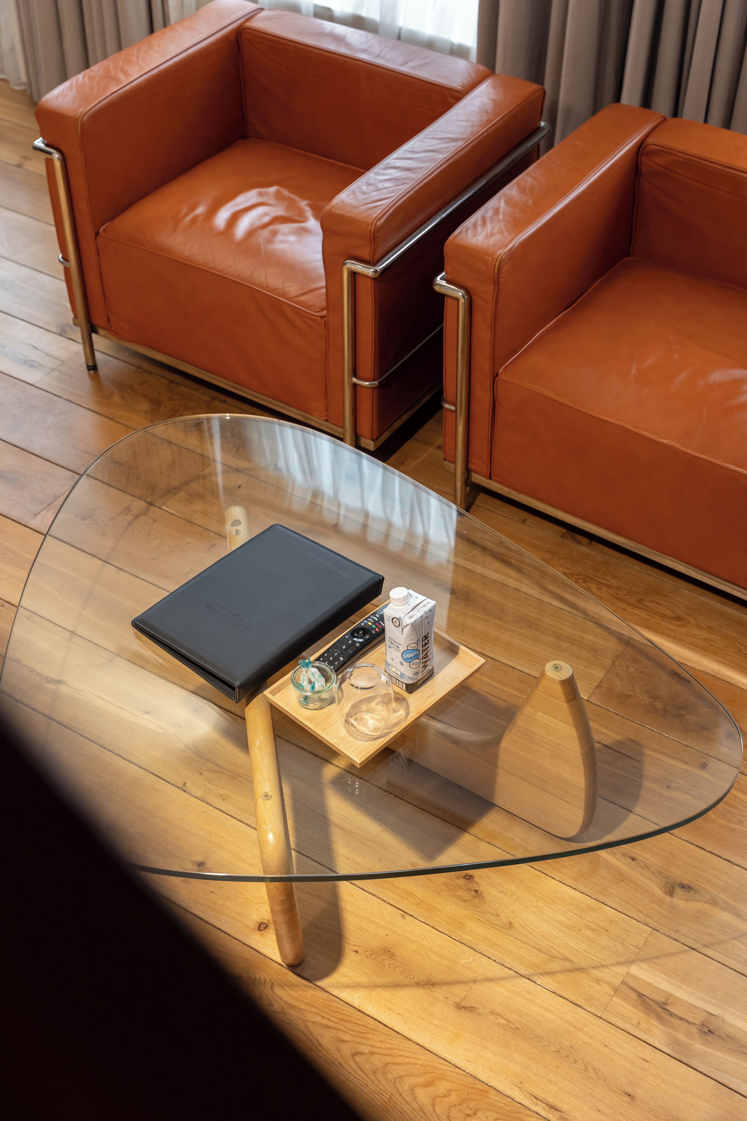 Una sala moderna con una mesa de centro de vidrio, sofá de cuero y piso de madera.