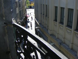 Vista desde un balcón sobre una calle empedrada con gente caminando y edificios.