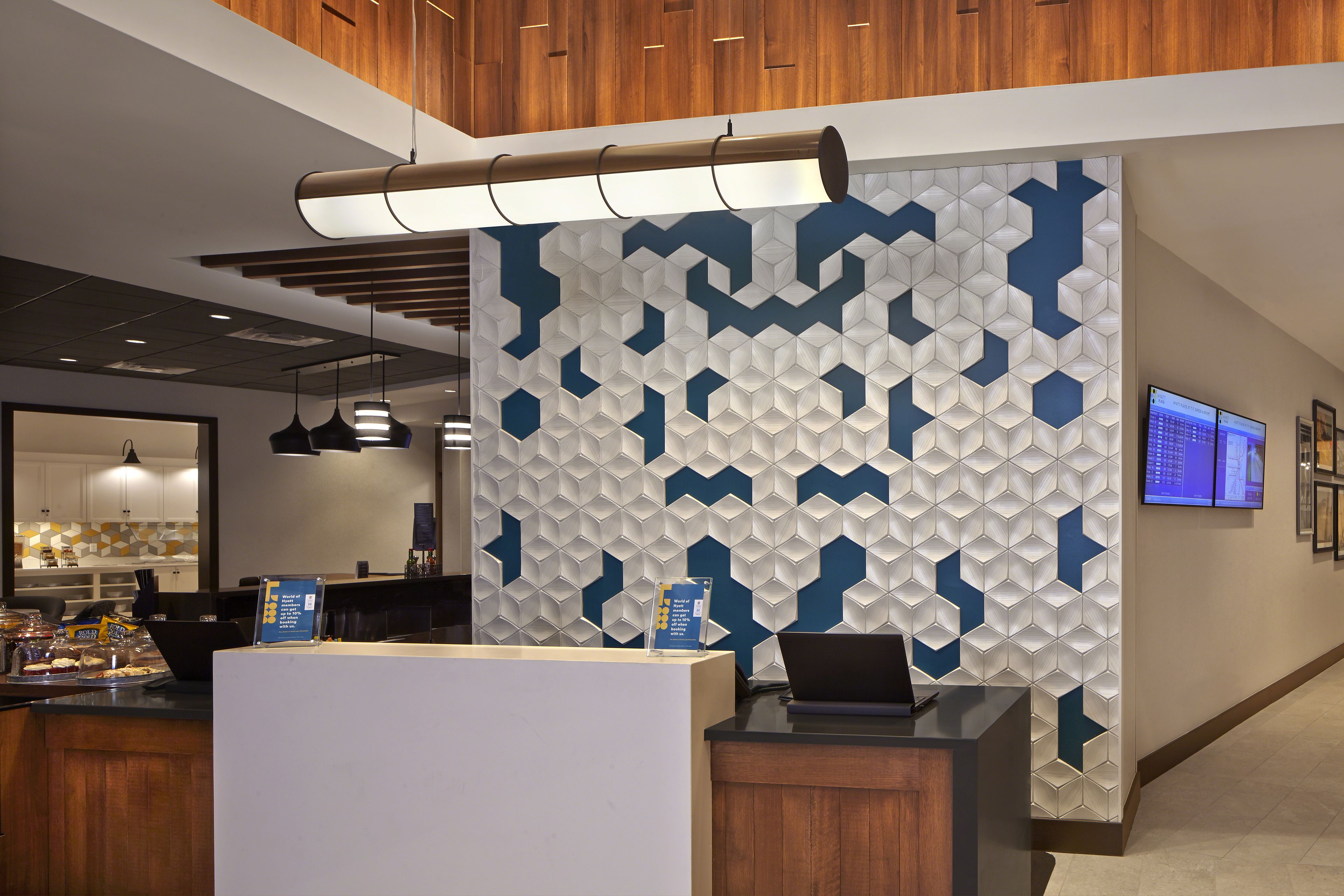 A reception area with a modern design, featuring a geometric patterned wall, a reception desk, and a digital screen displaying information.