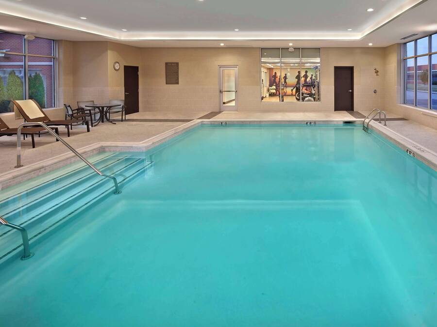 Una amplia piscina cubierta con sillas de descanso y una mesa, rodeada de paredes con ventanas y una puerta.