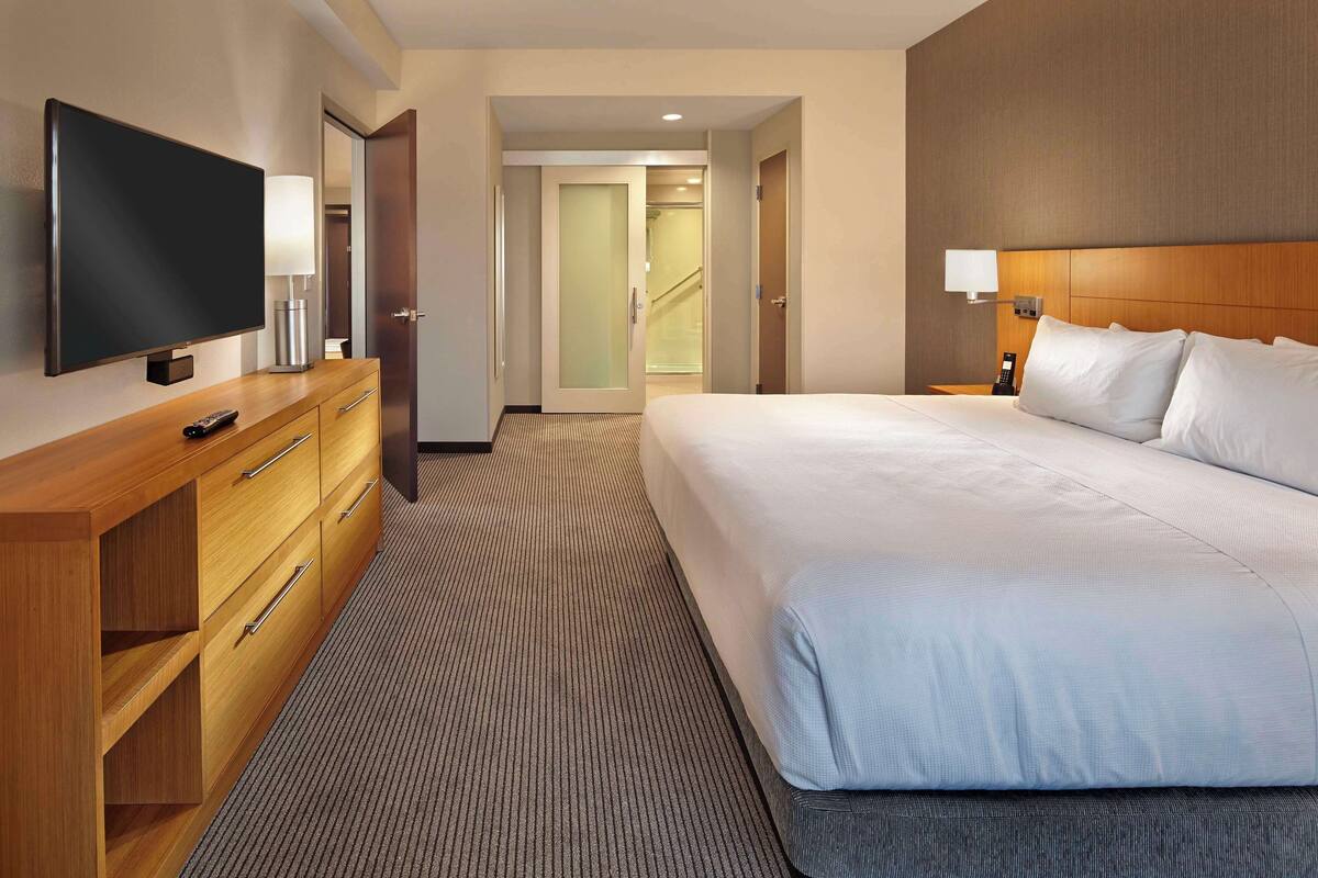Ein Hotelzimmer mit einem großen Bett, einem Fernseher auf einer Holzkommode, einem Schreibtisch mit Lampe und einer Treppe, die in einen anderen Raum führt.