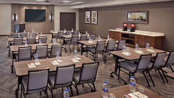 A conference room with multiple tables and chairs, equipped with water bottles, papers, and a coffee station.