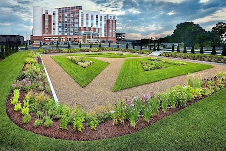 A hotel with a modern design, featuring a central garden with geometric landscaping and a parking area in front.