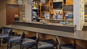 Un espace bar moderne doté d’un long comptoir, de tabourets et d’étagères remplies de bouteilles et de verres.