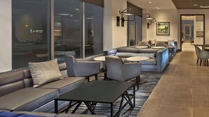 Eine moderne Hotellobby mit Ledersofas, runden Tischen und einem großen Fenster mit Blick auf die Stadt.