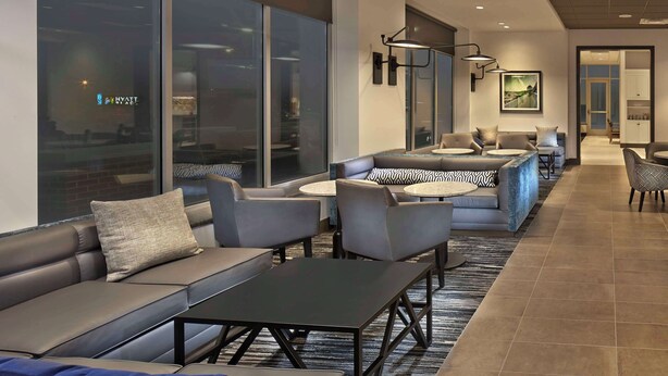 Un hall d’hôtel moderne, doté de canapés en cuir, de tables rondes et d’une grande fenêtre donnant sur la ville.