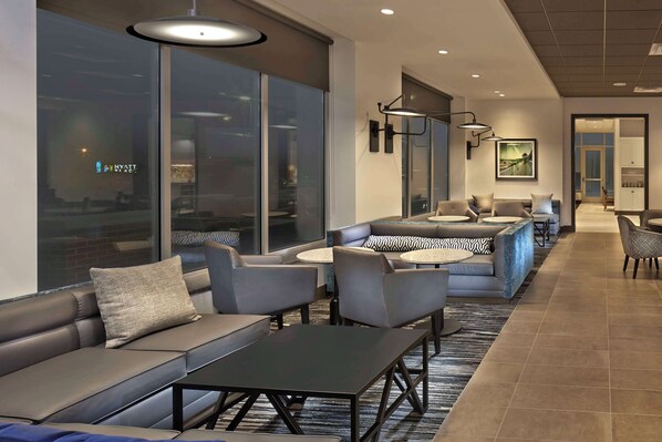 Eine moderne Hotellobby mit Ledersofas, runden Tischen und einem großen Fenster mit Blick auf die Stadt.