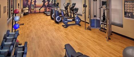 A gym with exercise equipment, a bench, and a wall with silhouettes of runners.