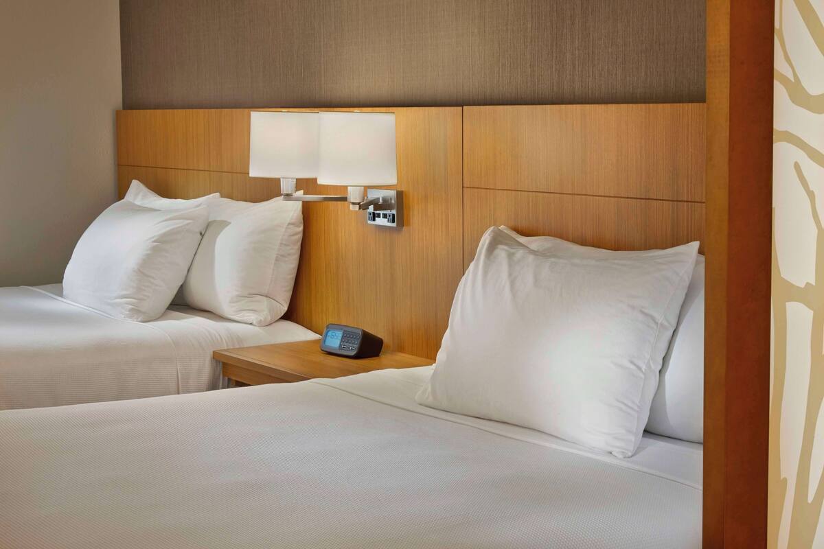 Ein Hotelzimmer mit zwei Betten, jeweils mit weißen Bettwäsche und Kissen, einem hölzernen Kopfteil und einem Nachttisch mit einer Uhr.