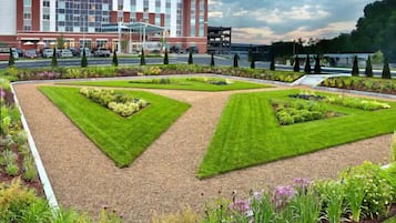 Un hotel con diseño moderno, que cuenta con un patio central con césped y parterres de flores cuidados, rodeado por un estacionamiento y una carretera.