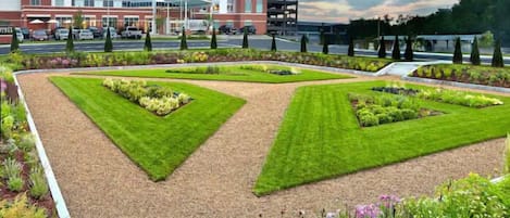 A hotel with a modern design, featuring a central courtyard with neatly trimmed grass and flower beds, surrounded by a parking area and a road.