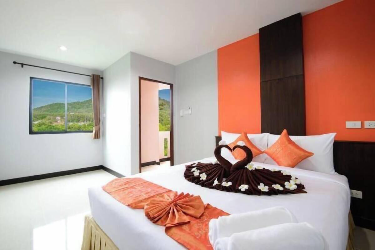 Habitación de hotel con una cama grande, vistas a zonas verdes y un diseño moderno con paredes color naranja y blanco.