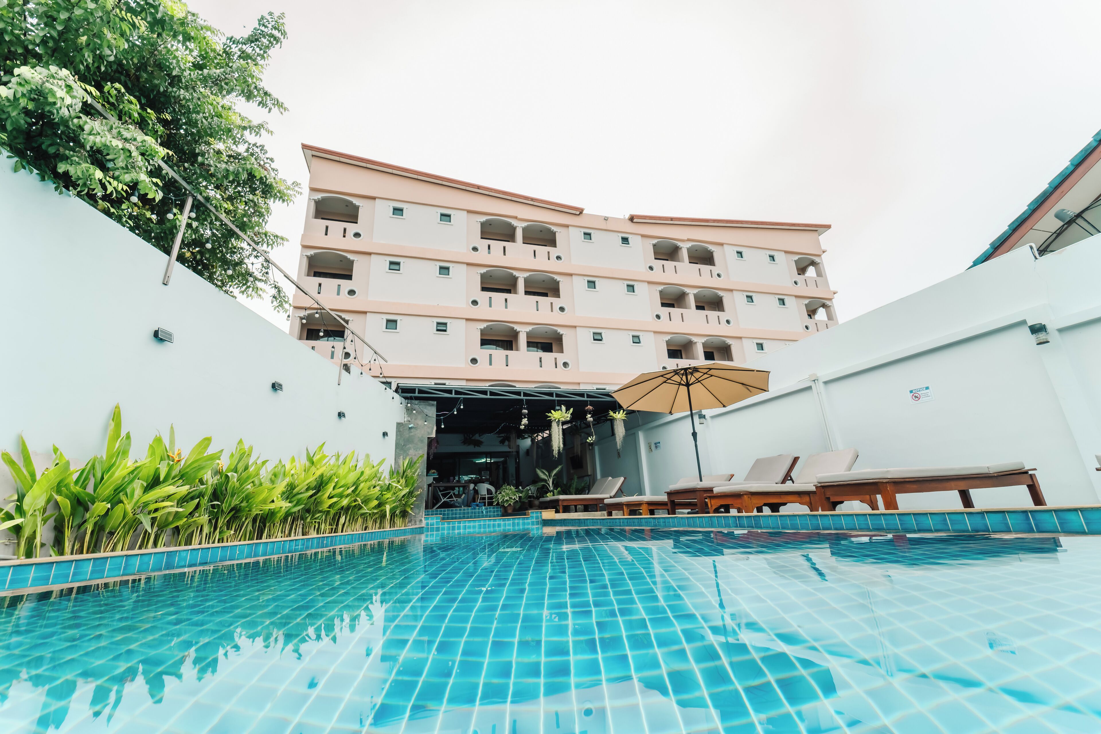 A swimming pool with lounge chairs and umbrellas, surrounded by a building with multiple balconies.